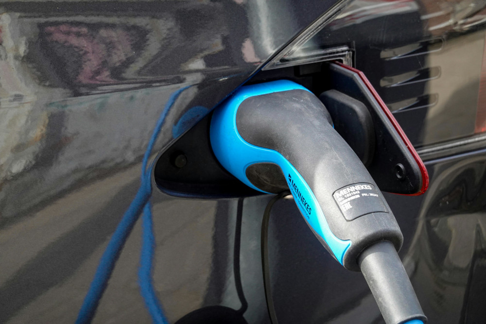 Close-up of a blue and black Mennekes electric vehicle charging plug inserted into a dark grey car's charging port.